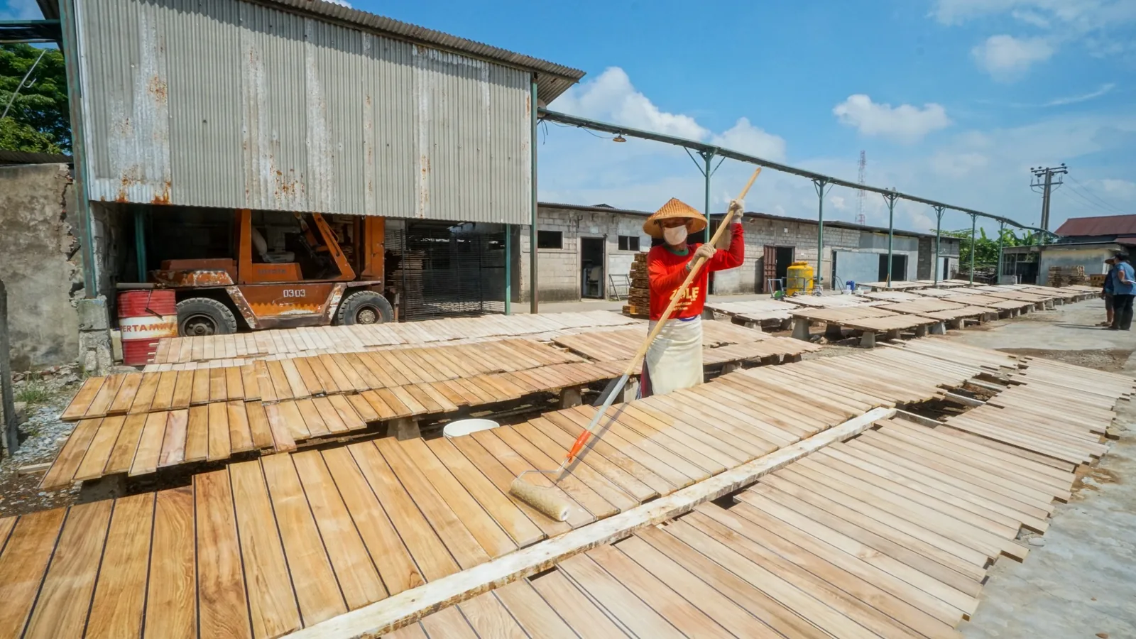 A craftsperson applying finish to rows of wooden pieces in open air